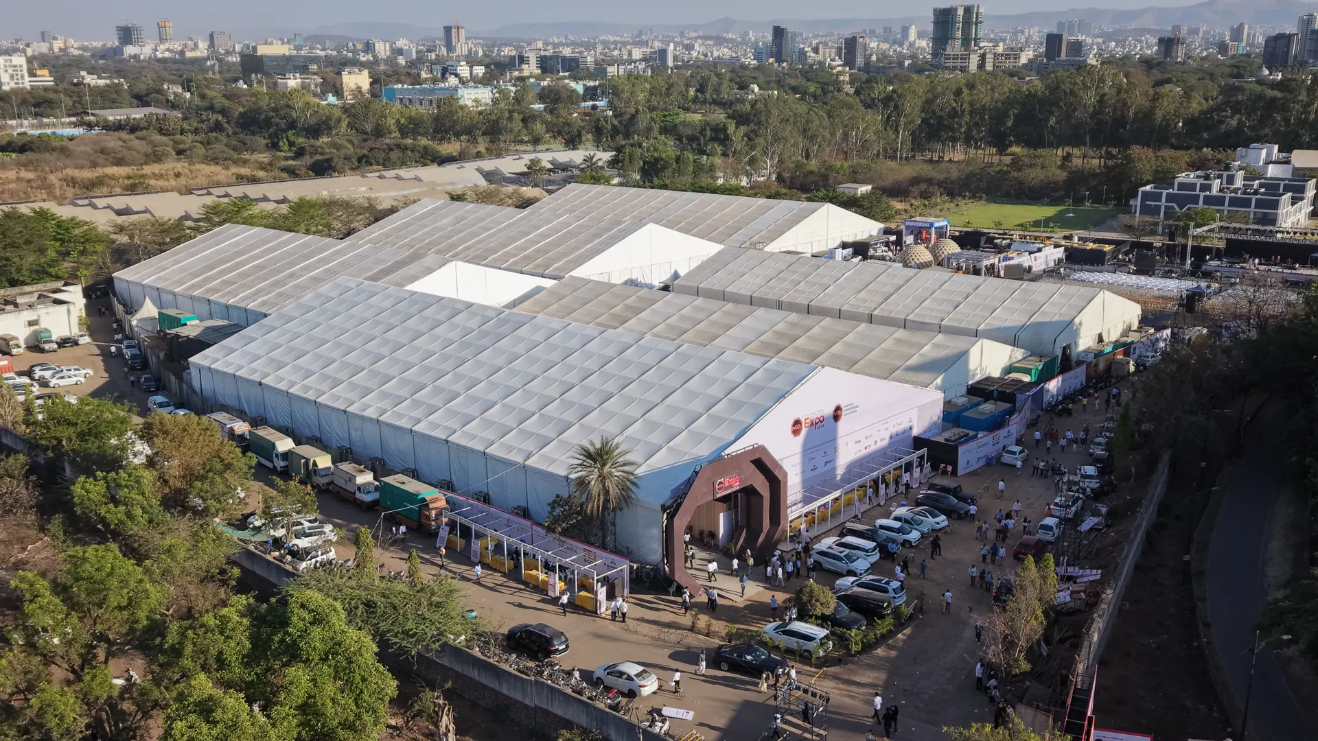 Aerial view of a trade expo's exhibition halls, with visitors arriving at the entrance arch