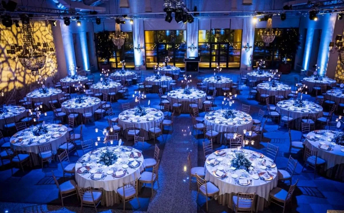 A ballroom set with round tables under blue uplighting and chandeliers