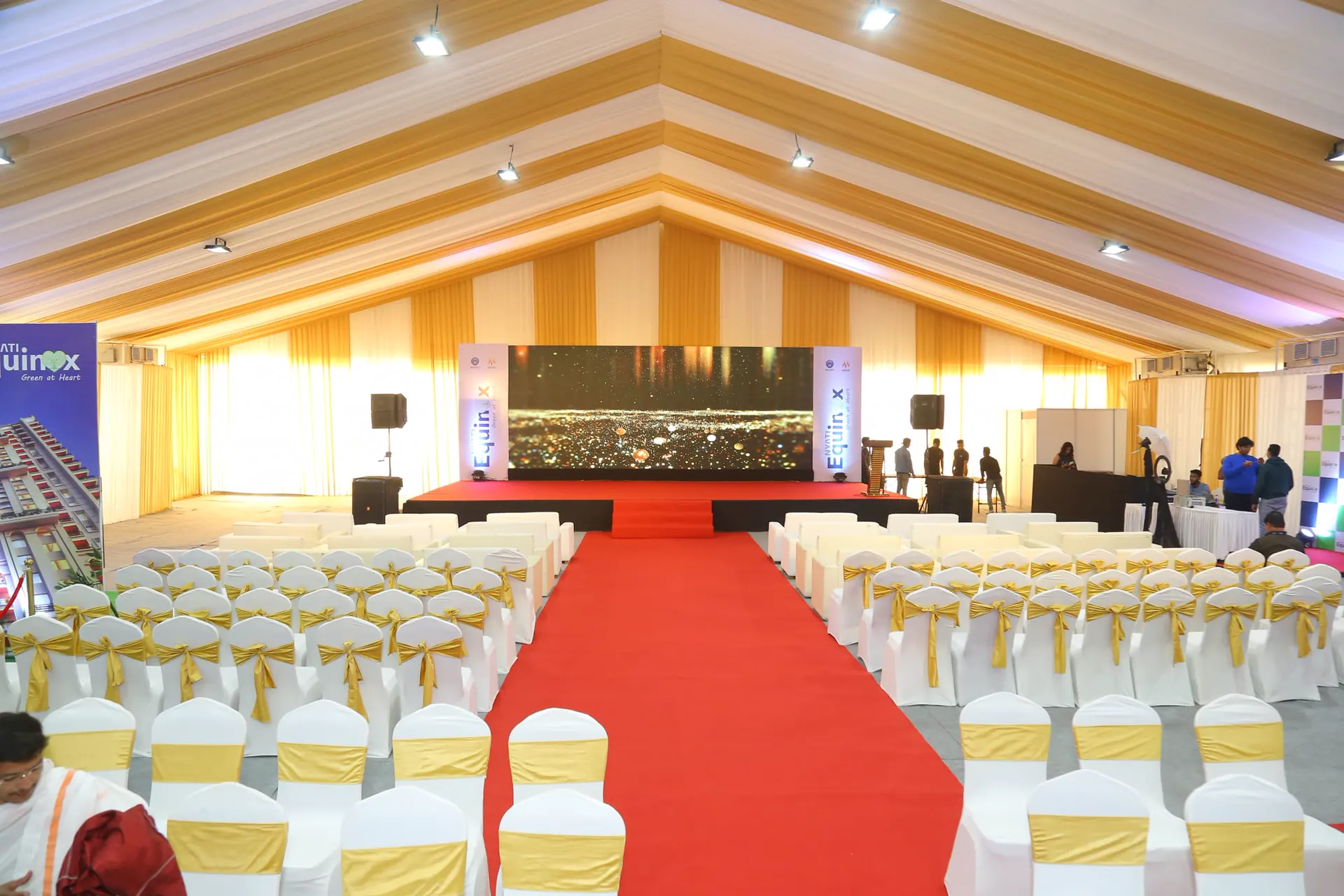 A large covered hall set with a stage, LED screen, aisle and rows of seating