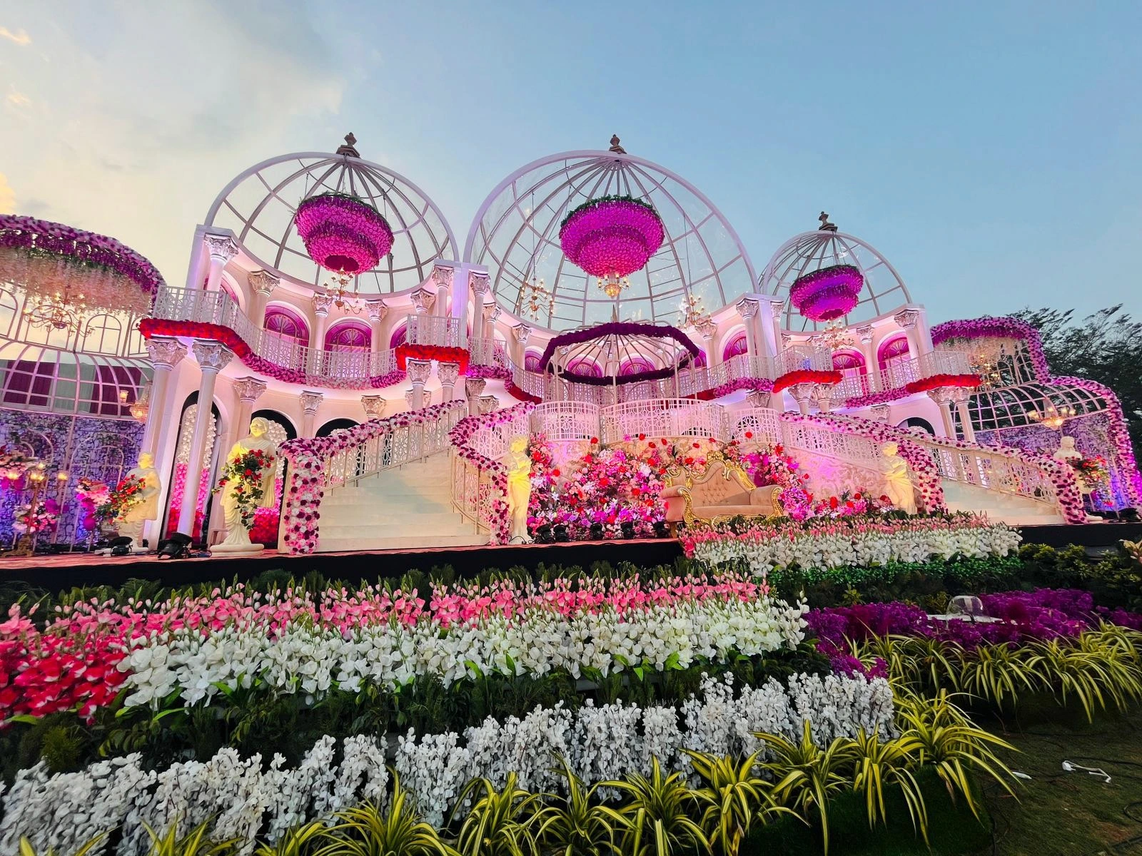 A domed wedding stage with floral chandeliers, banked with rows of orchids and roses